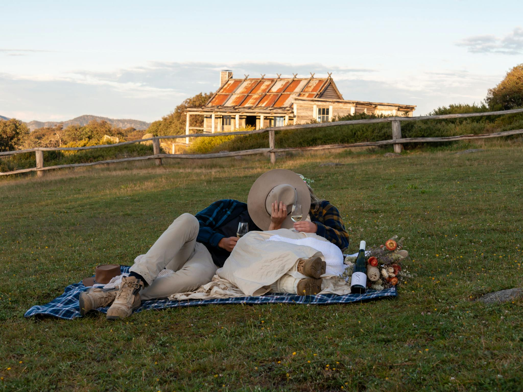 Just married couple relaxing on a picnic blanket in front of Craig's Hut with a glass of wine.