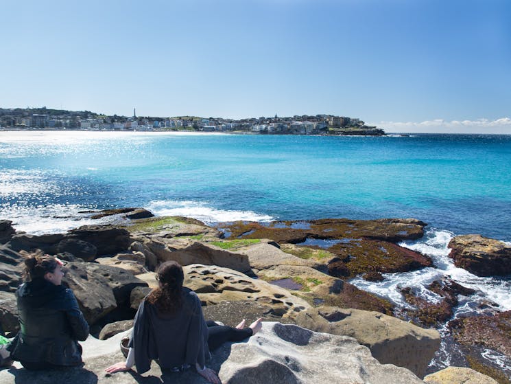 Two friends sit on the rocks to watch the waves roll in at Bondi beach