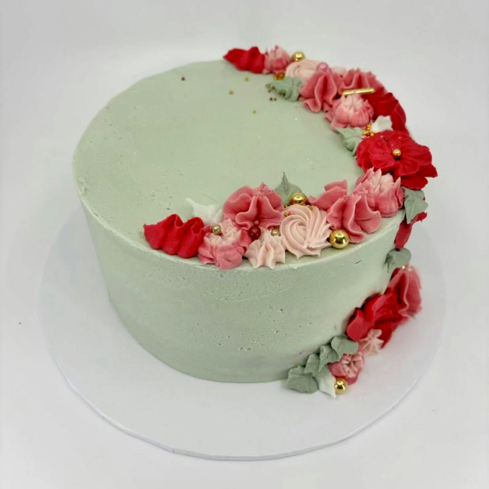 a sage green cake with shades of pink piping on the top and own the sides