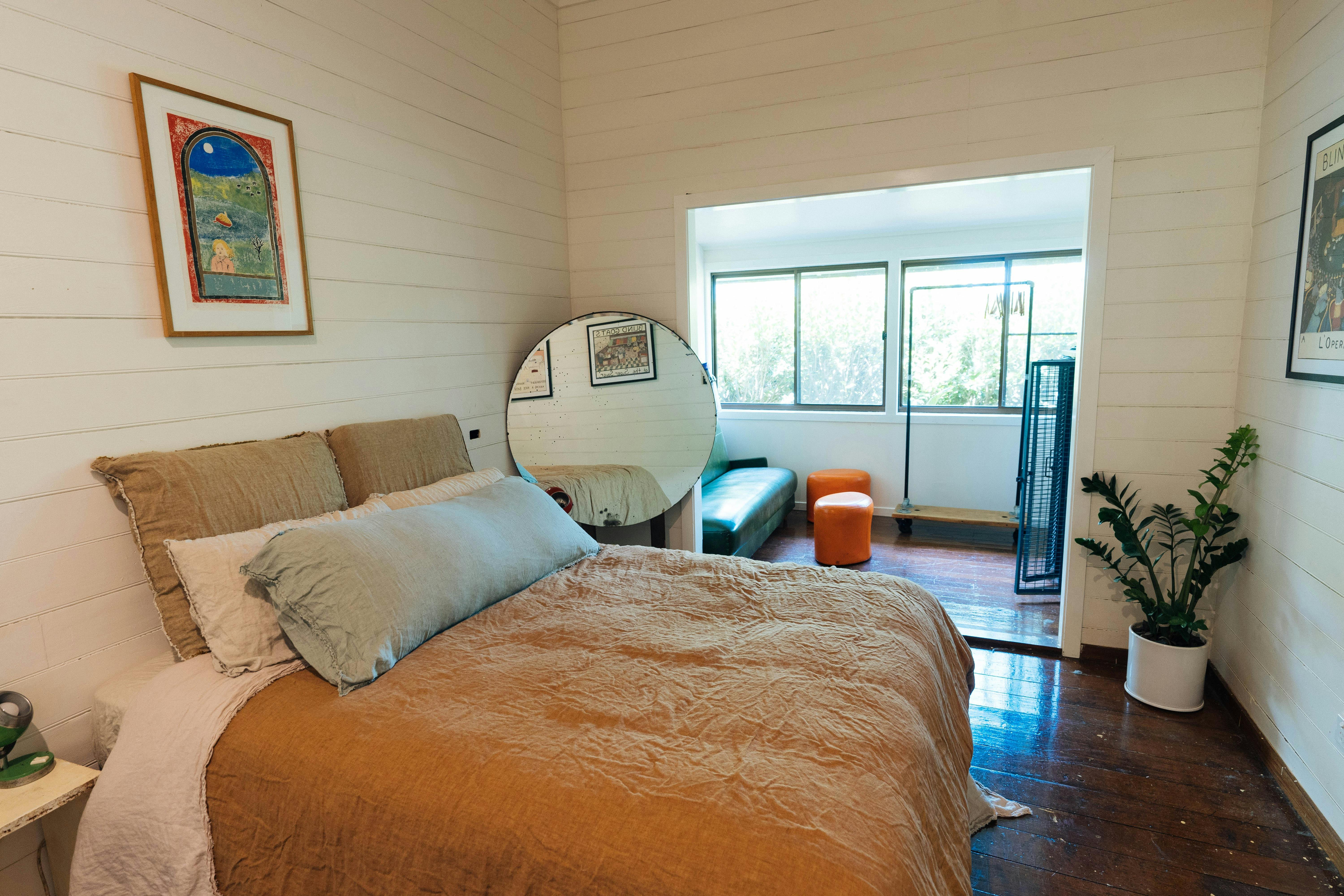 A bedroom with large queen sized bed and European linen sheets. A large round mirror, a sitting room