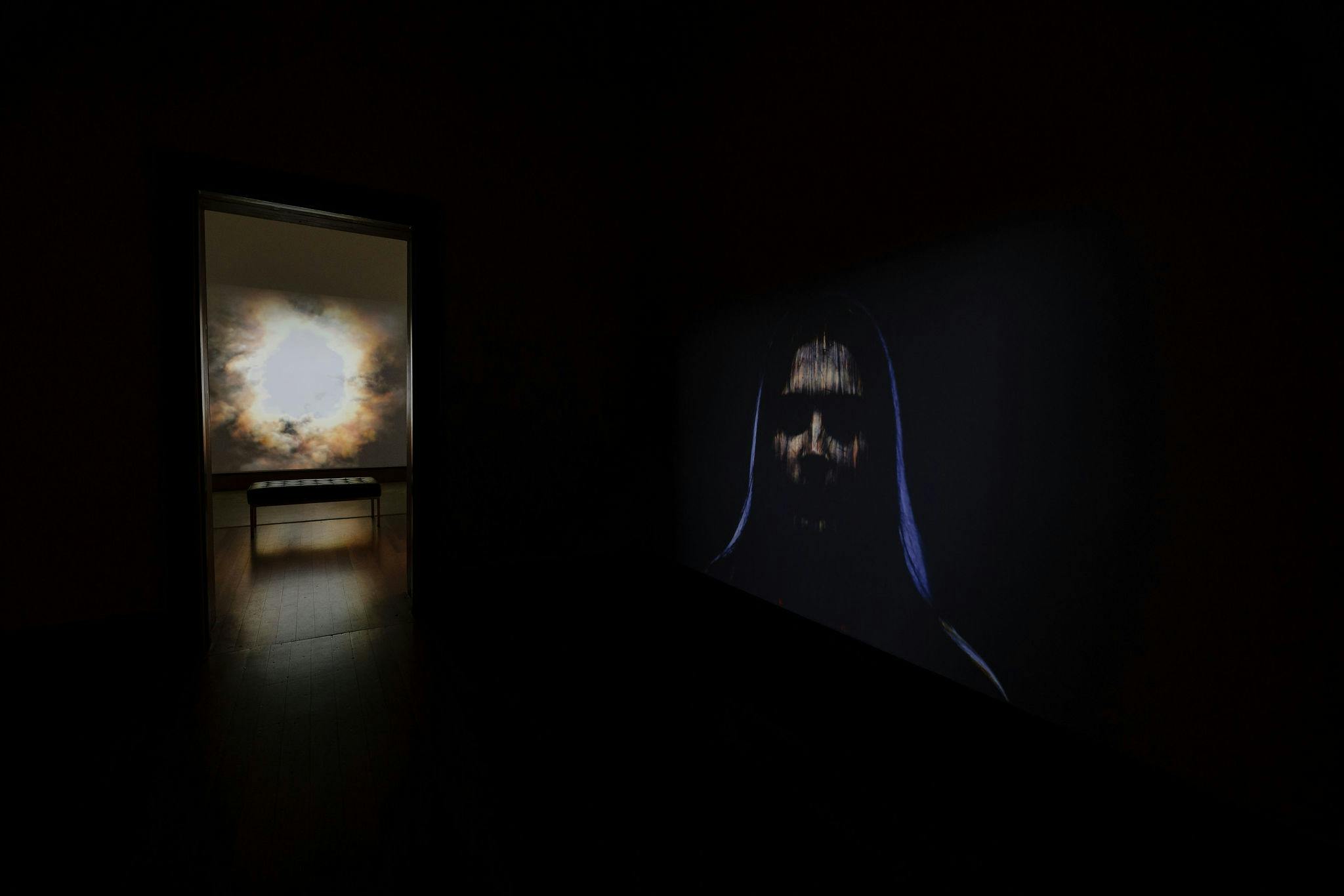 A veiled woman and supernova appear on two screens, situated in two adjacent galleries .