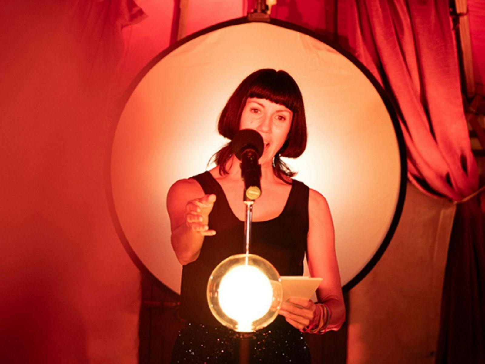 Megan Drury performing in an illuminated space with red drapes