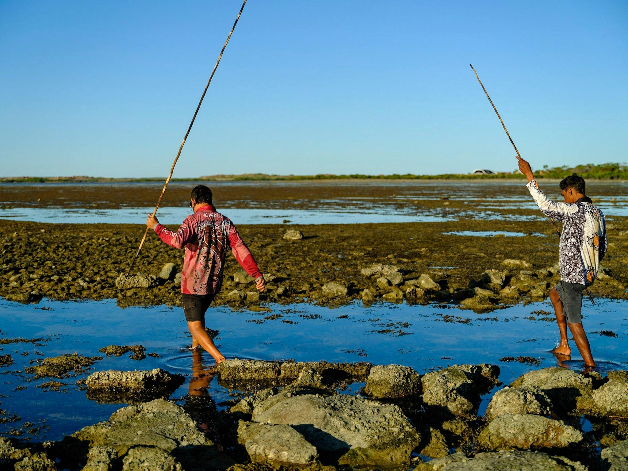 Two boys walking in mangroves with colourful bushshirts and spears.