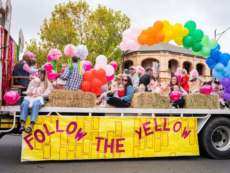 A group of children and adults on the back of a truck with the sign Follow the Yellow Brick Road.
