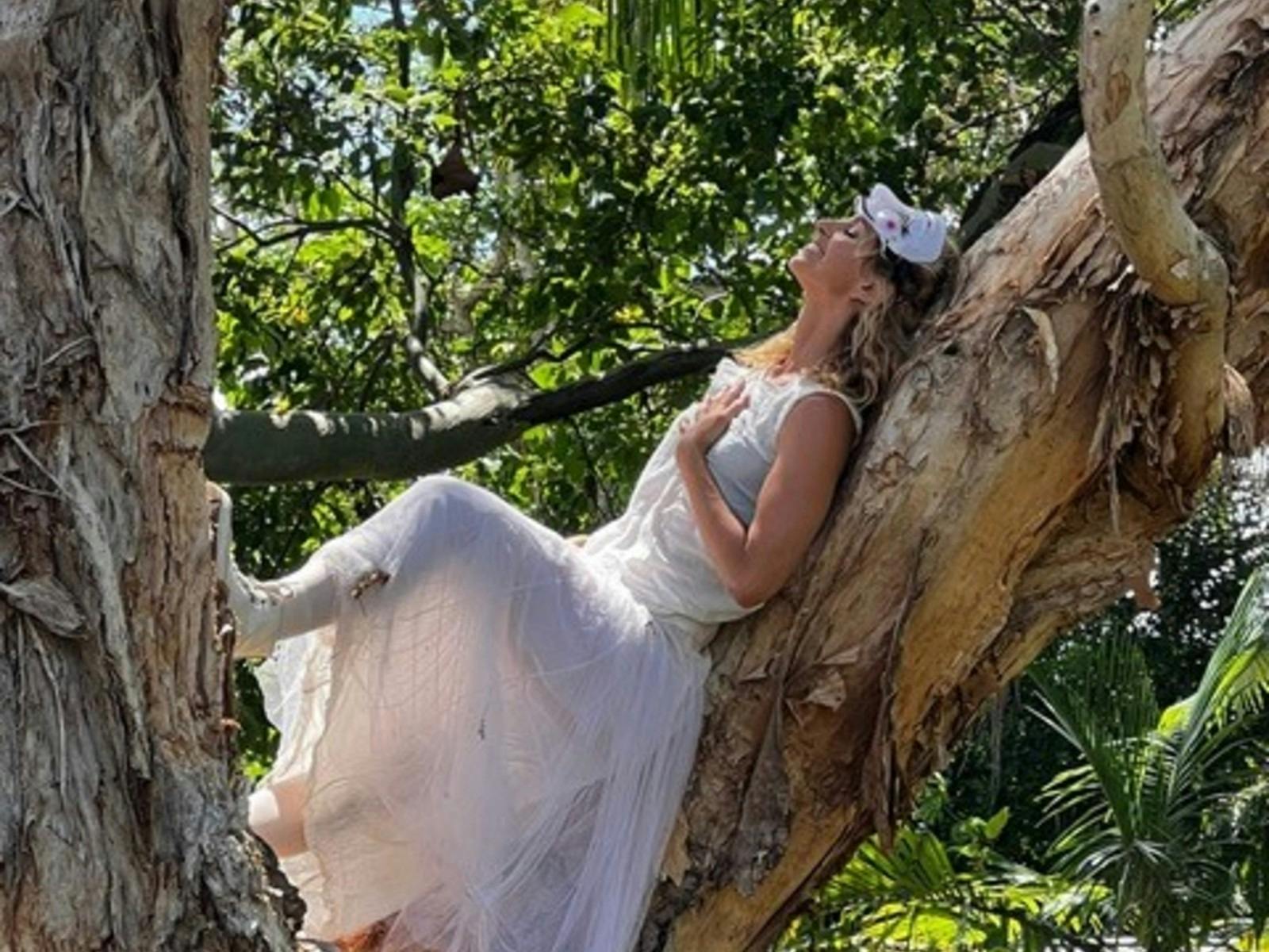 Female performer lying on tree branch with white dres