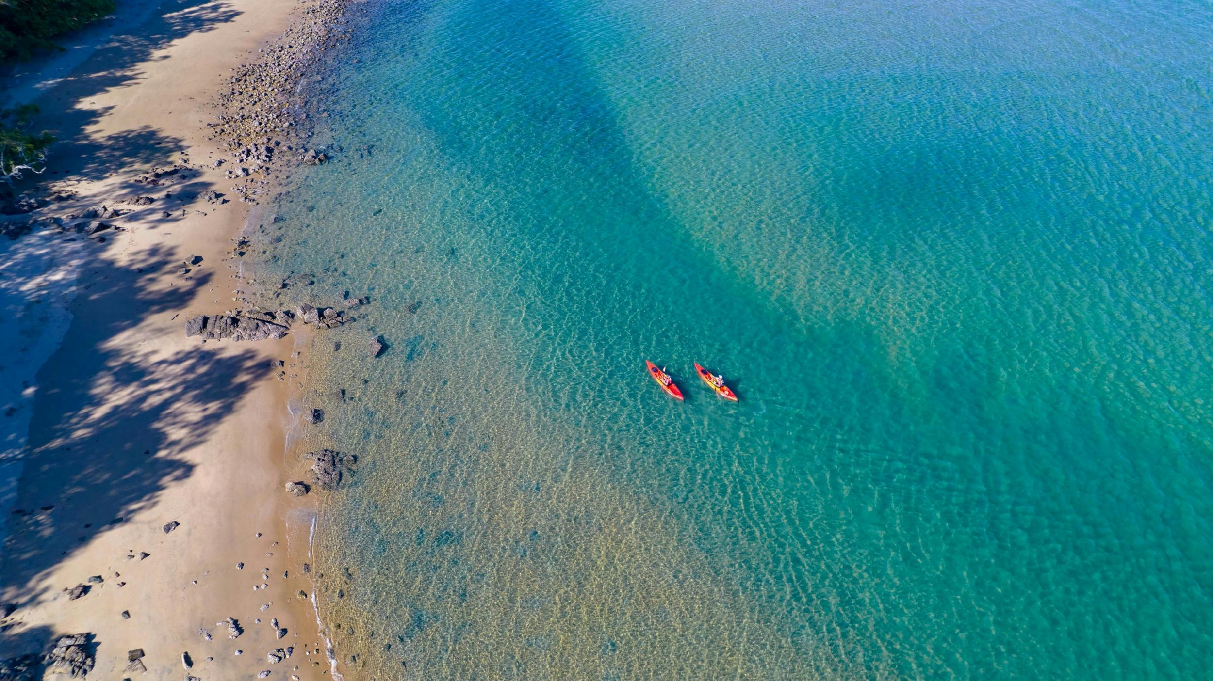Aerial photo of two kayaks paddling along the shore in turquoise water