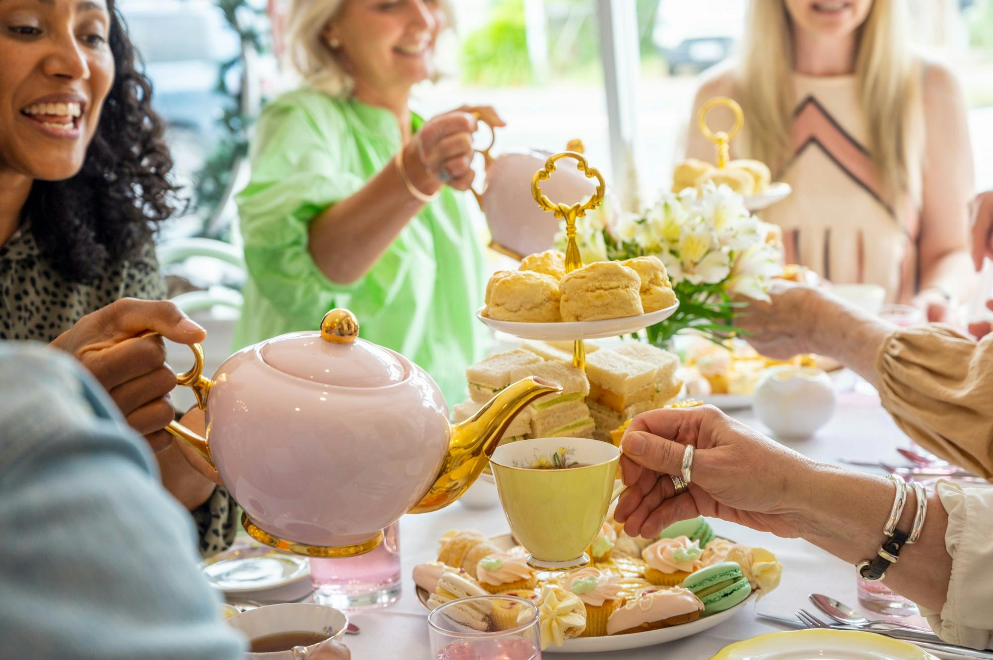 A group of women having high tea with cups of tea and finger food