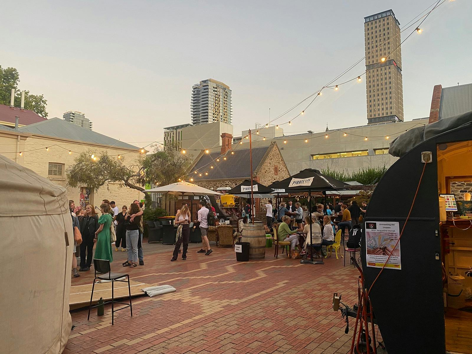 A brick courtyard with people waiting to enter a yurt for a performance.