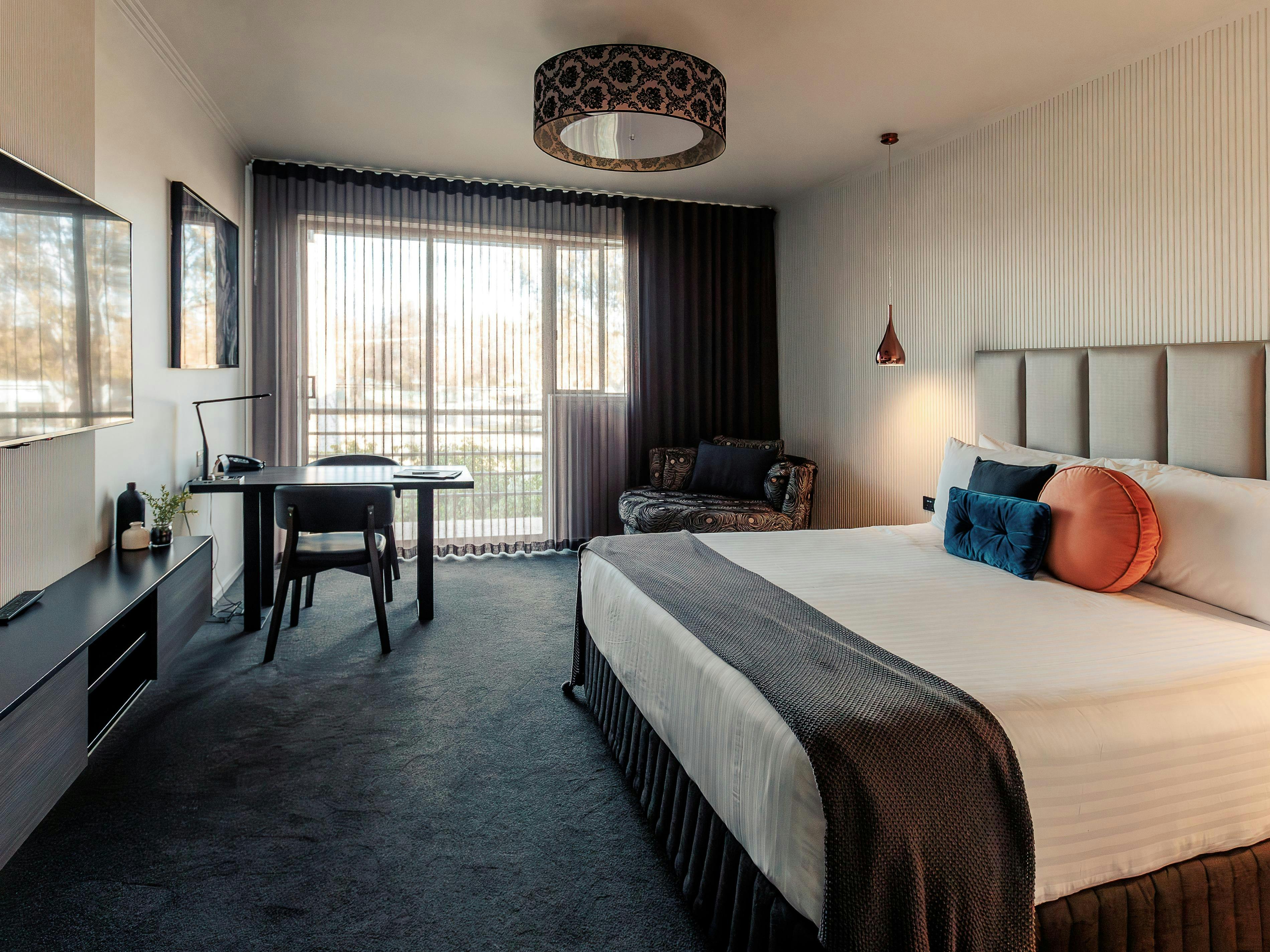 Accommodation room with bed, couch, small dining table and television looking out to a balcony view.
