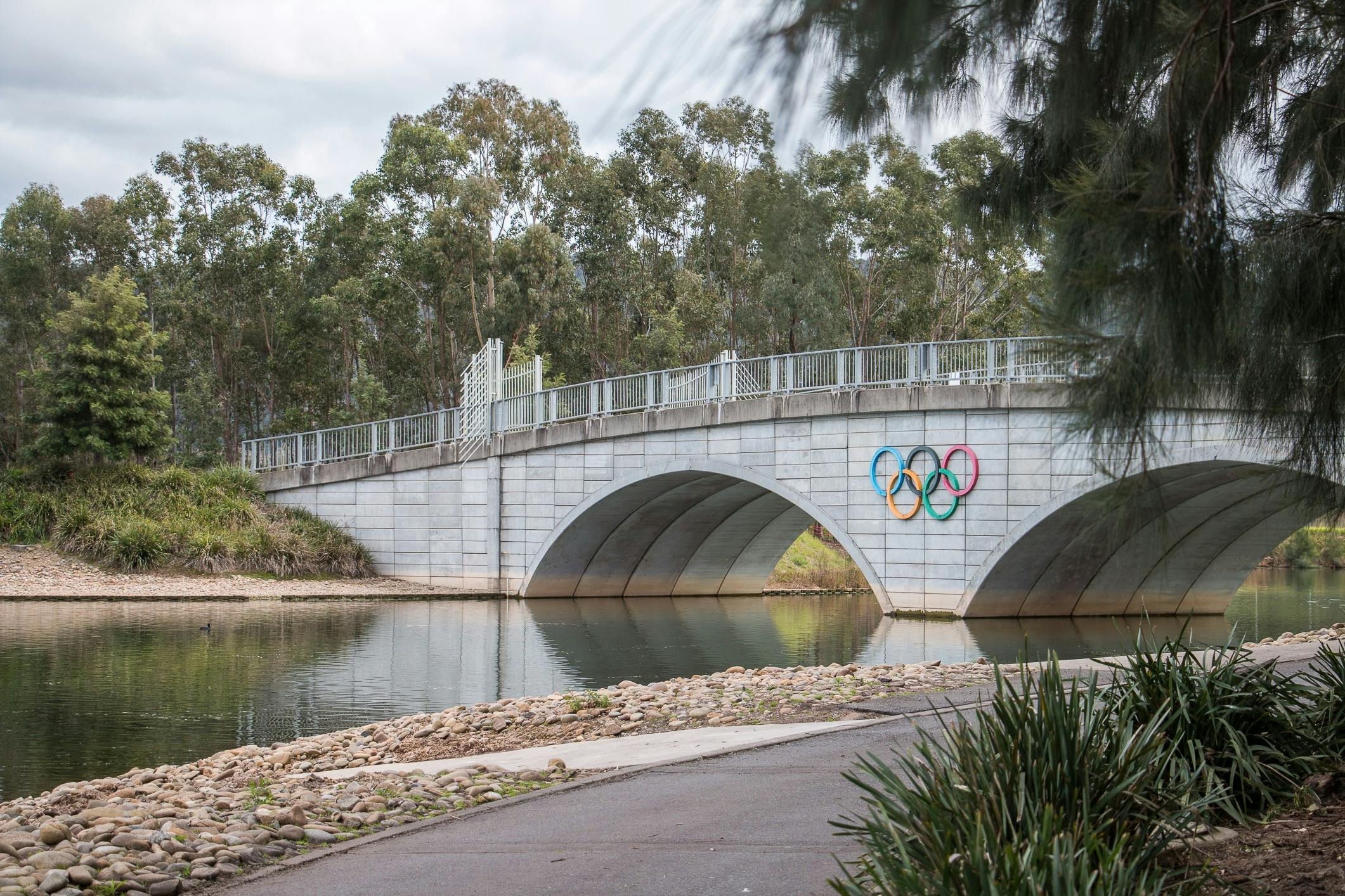 A rowing lake is pictured with a bridge housing the Olympic rings are present.