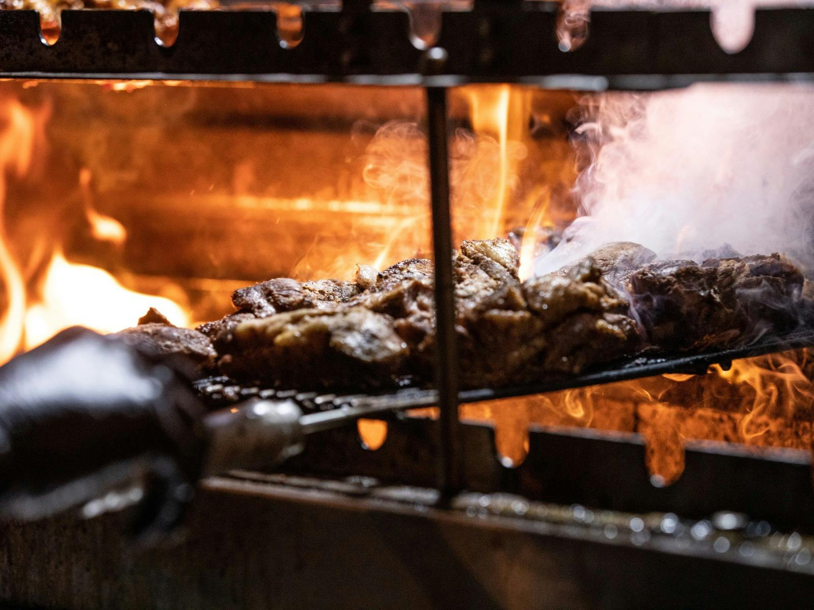 Meat grilling over open flames, with smoke rising from a barbecue pit.