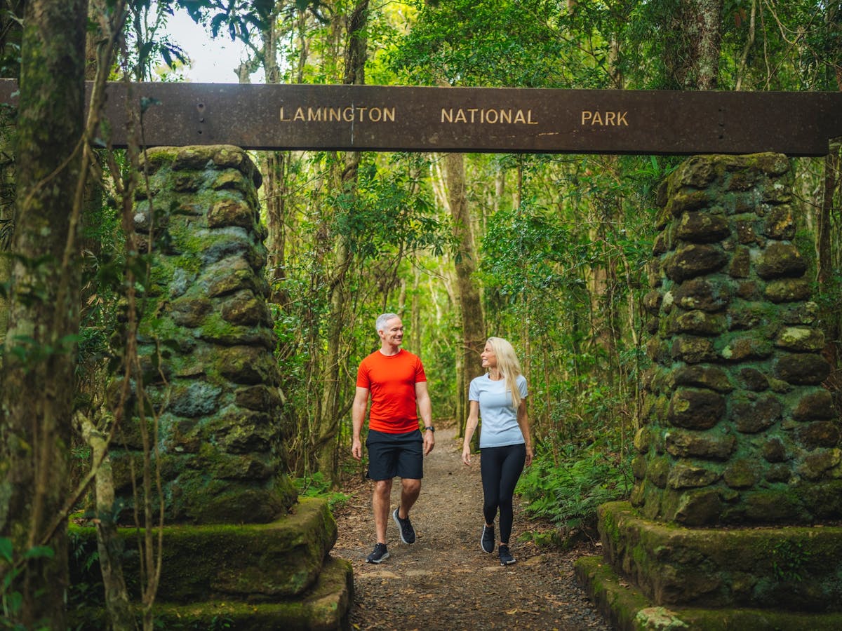 A man and woman walk through the arch at the start of a walk in a national park rainforest