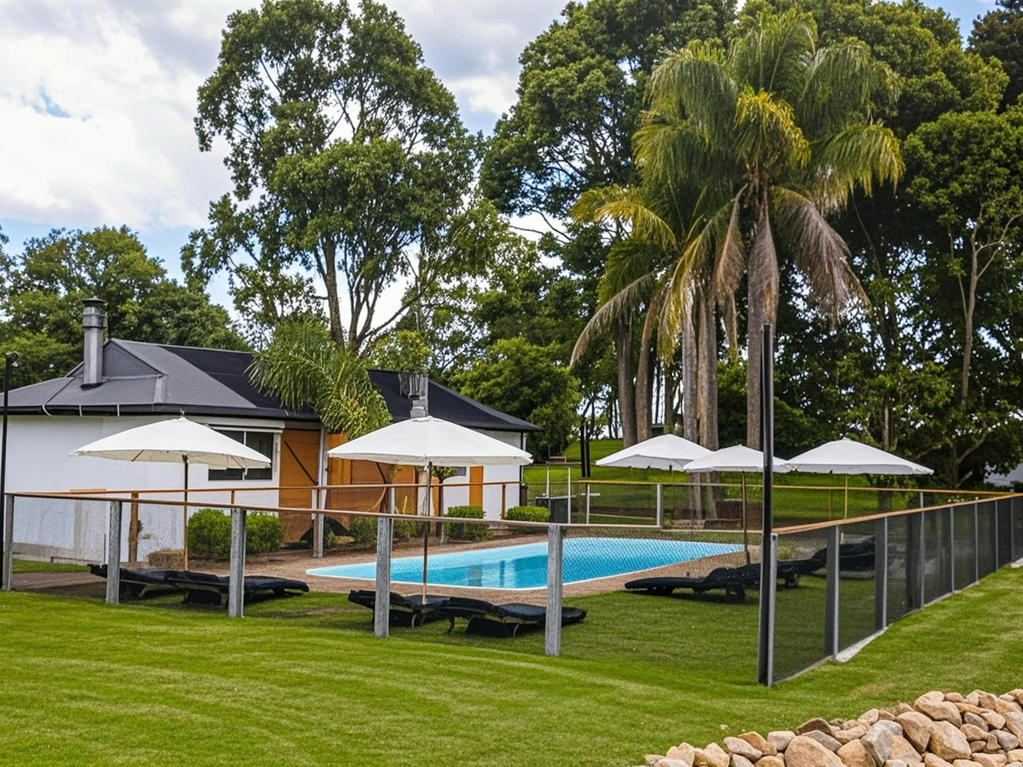 Solar heated pool at Eight Acres with sun loungers, umbrellas and palm trees and cottages