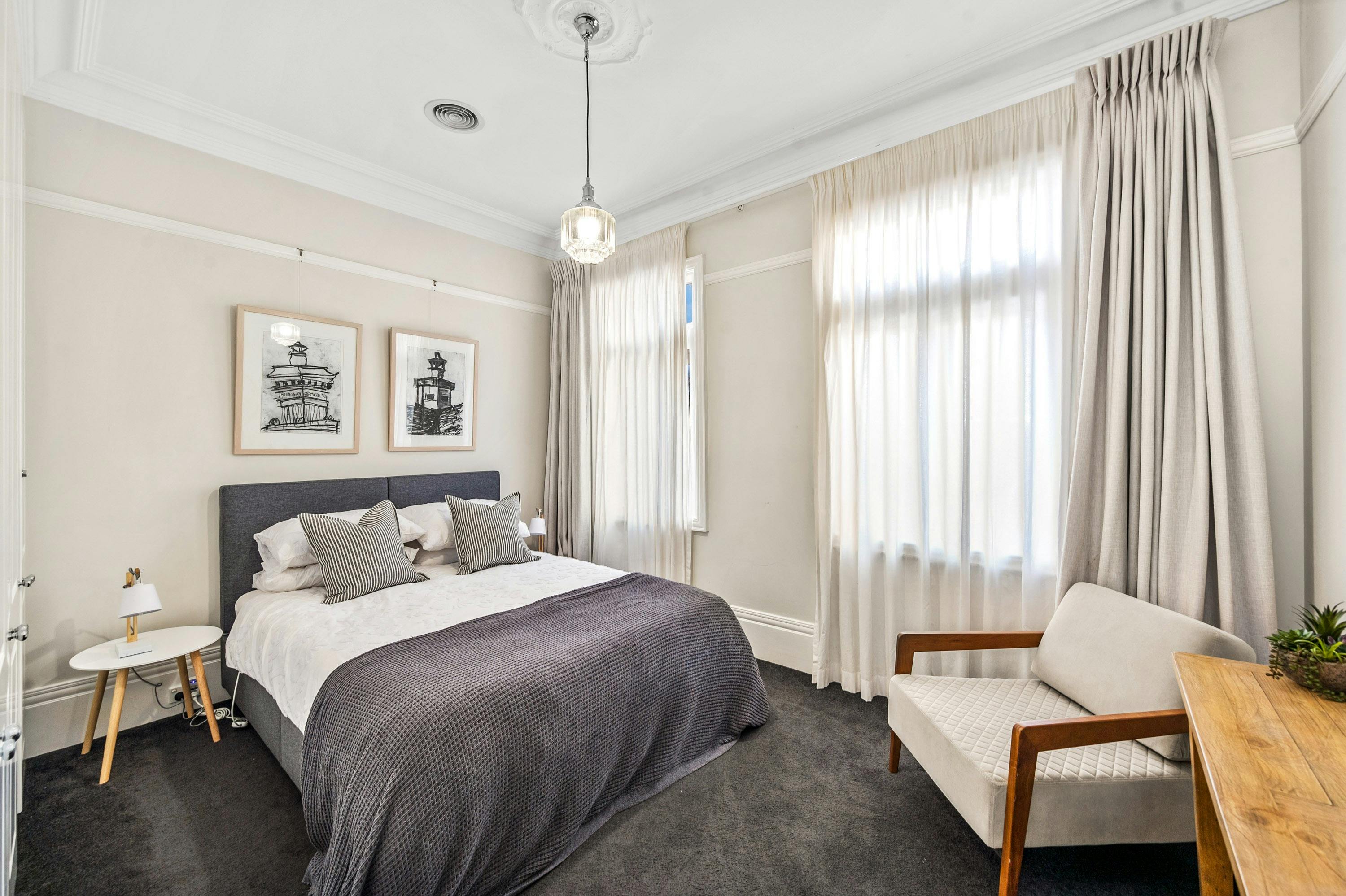 large bed, grey quilt, beige curtains, occasional chair