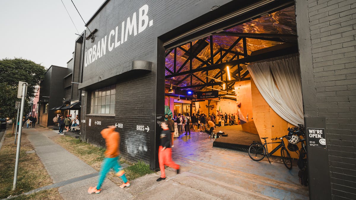 A black painted brick building, the facade of which says "Urban Climb." at the roller door entrance