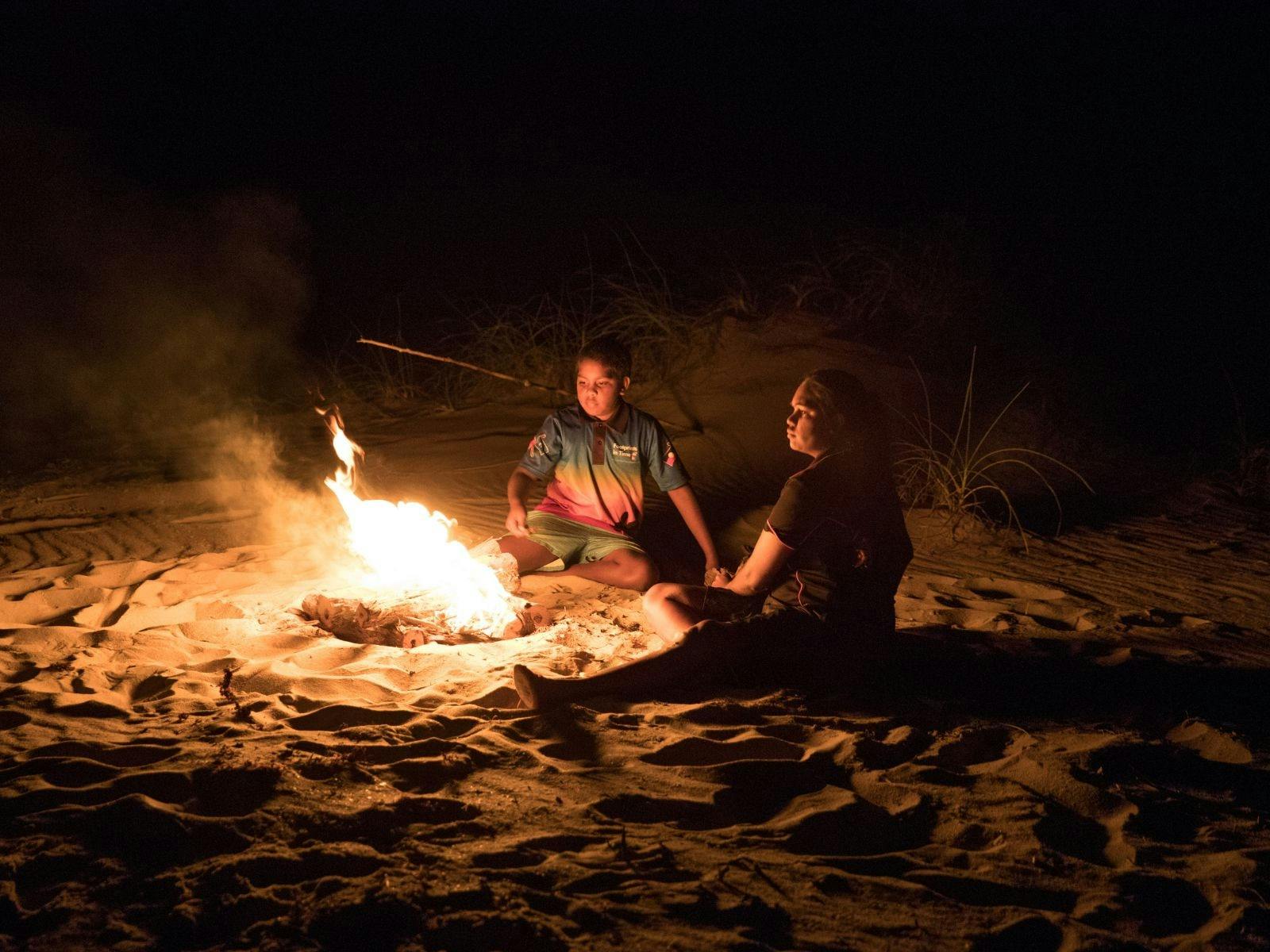 Two people sitting around a campfire talking.