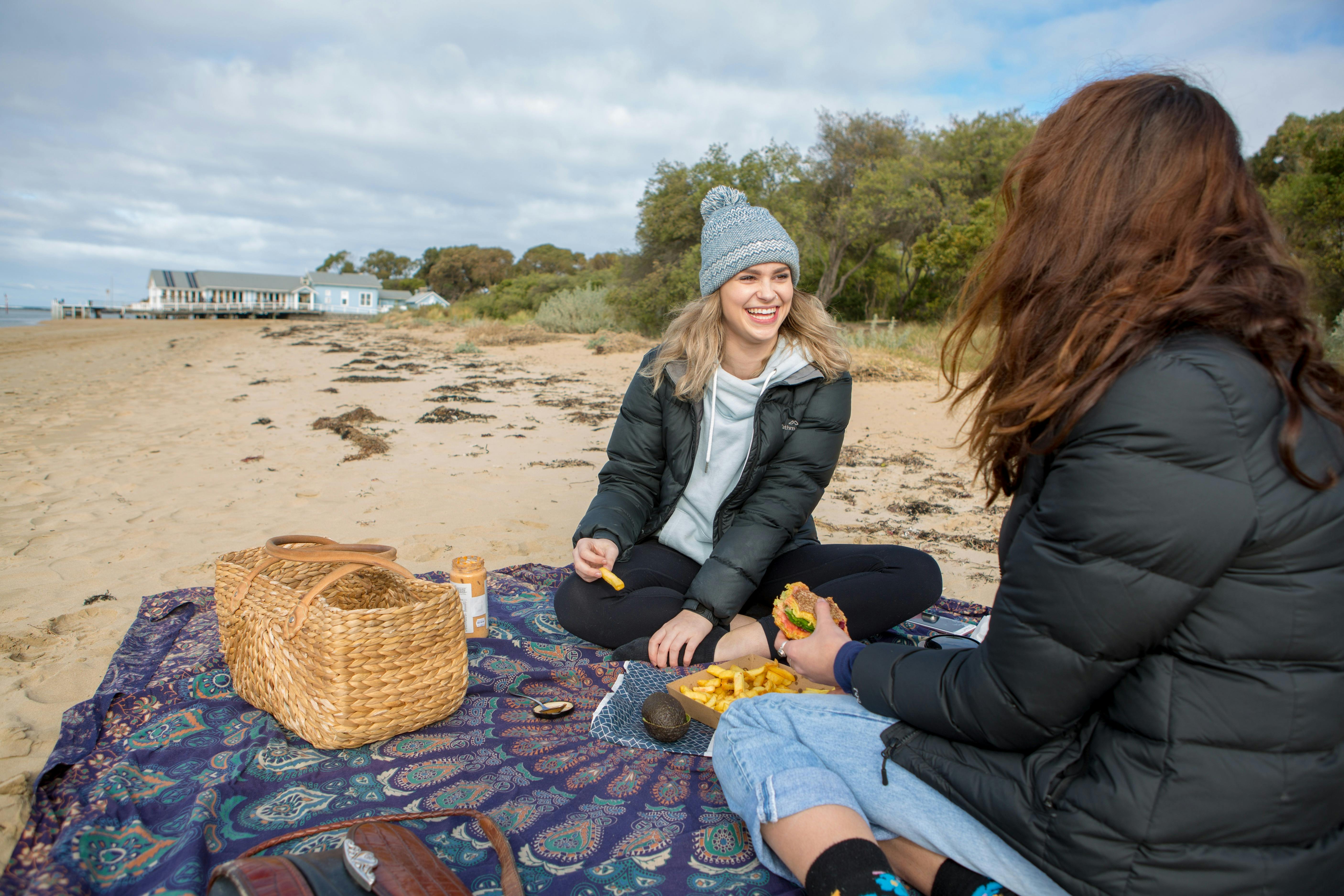 Two young women having a  beach picnic in the cooler months on the shores of the Barwon River