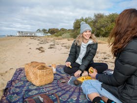 Two young women having a  beach picnic in the cooler months on the shores of the Barwon River