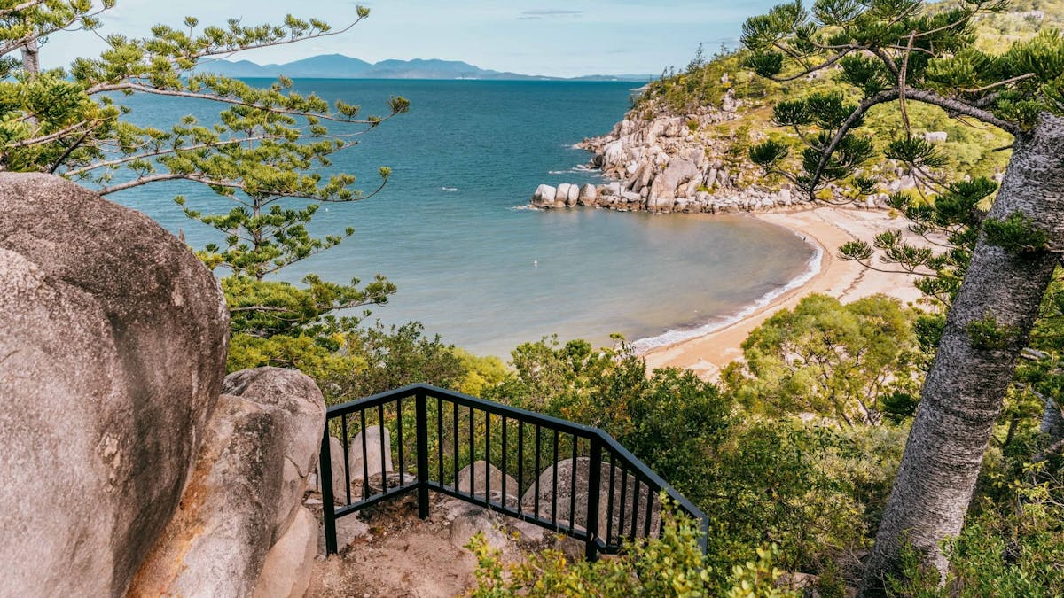 Looking down on a bay with hoop pine-clad granite headland and ocean and mountains in the background