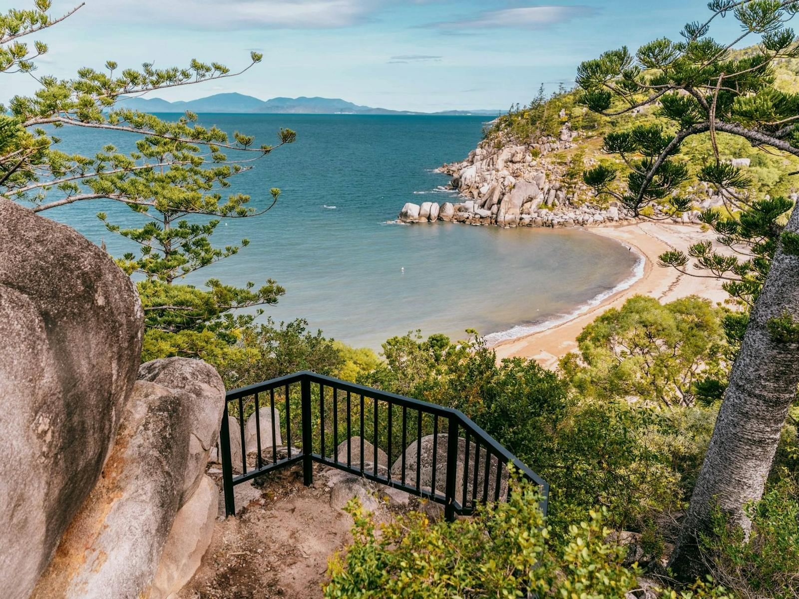 Looking down on a bay with hoop pine-clad granite headland and ocean and mountains in the background Looking down on a bay with hoop pine-clad granite headland and ocean and mountains in the background