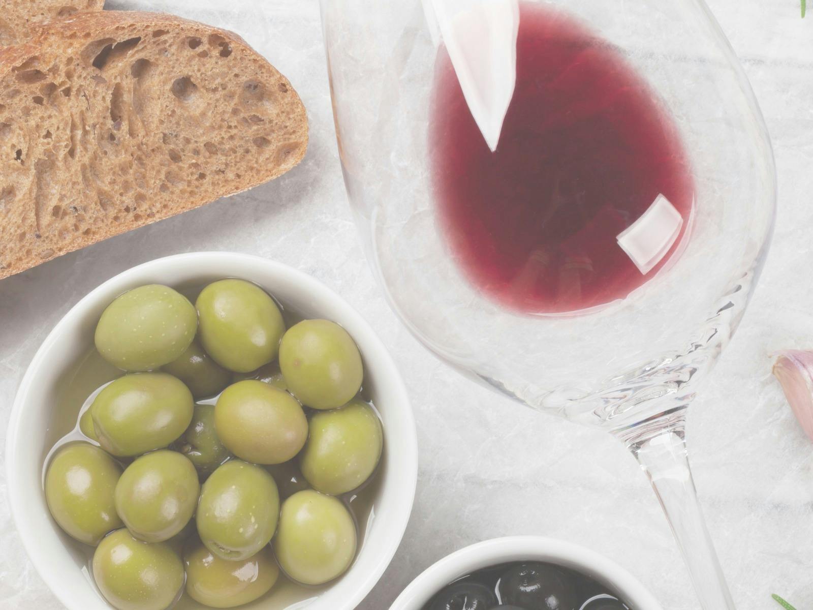 Olives, bread and red wine in a glass on a white table