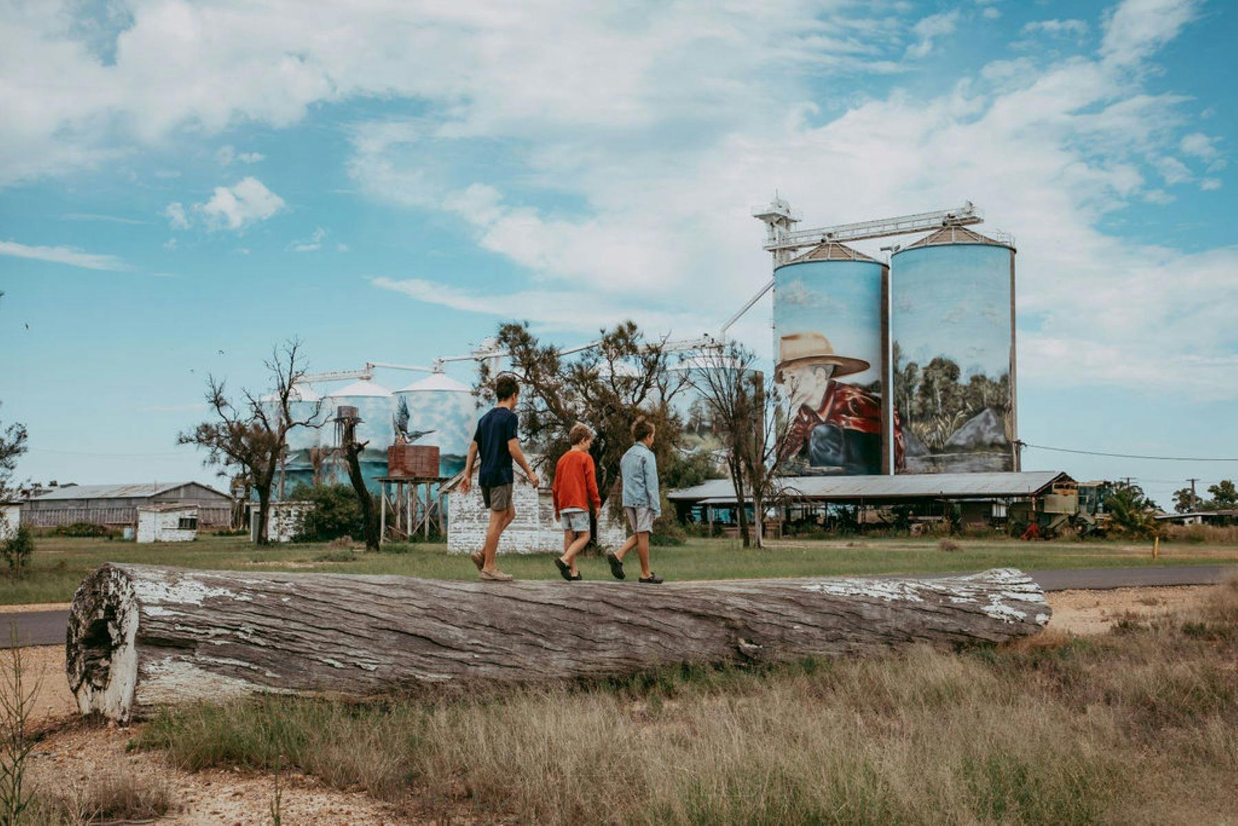 Children walking across a log in front of the Yelarbon Silos