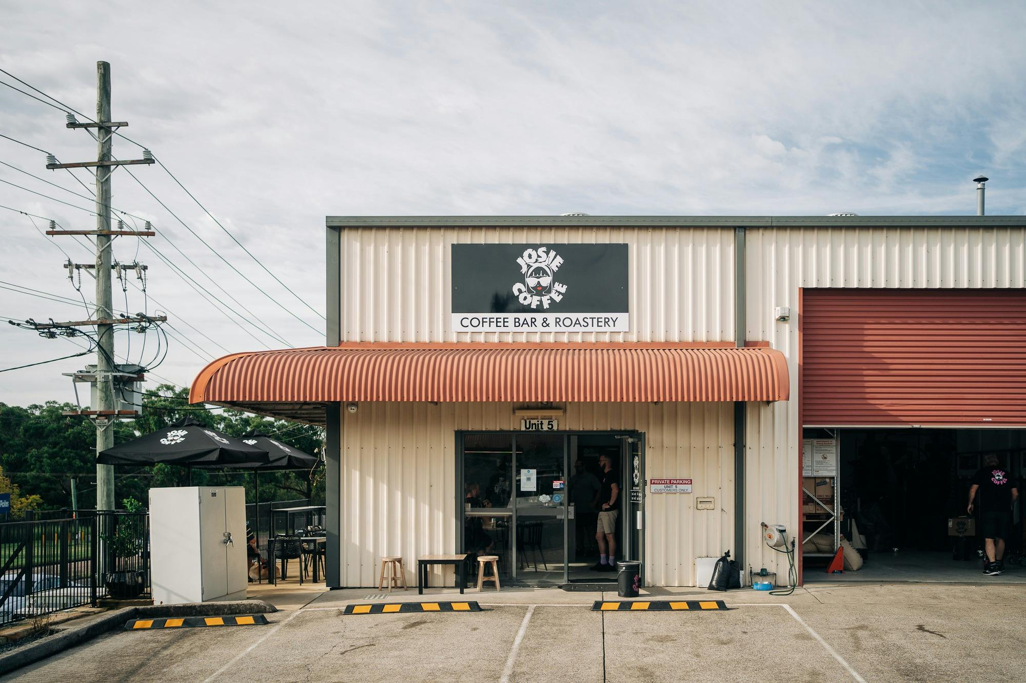 The front of the café as seen from the parking. The roller door to the roastery is open,