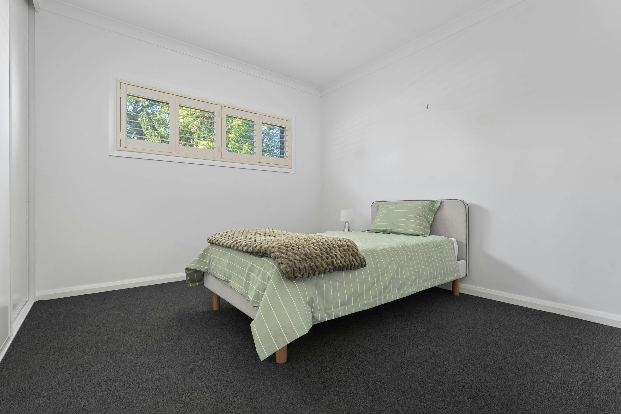 Single bed with green bedding, including a green throw, grey bed head and high window