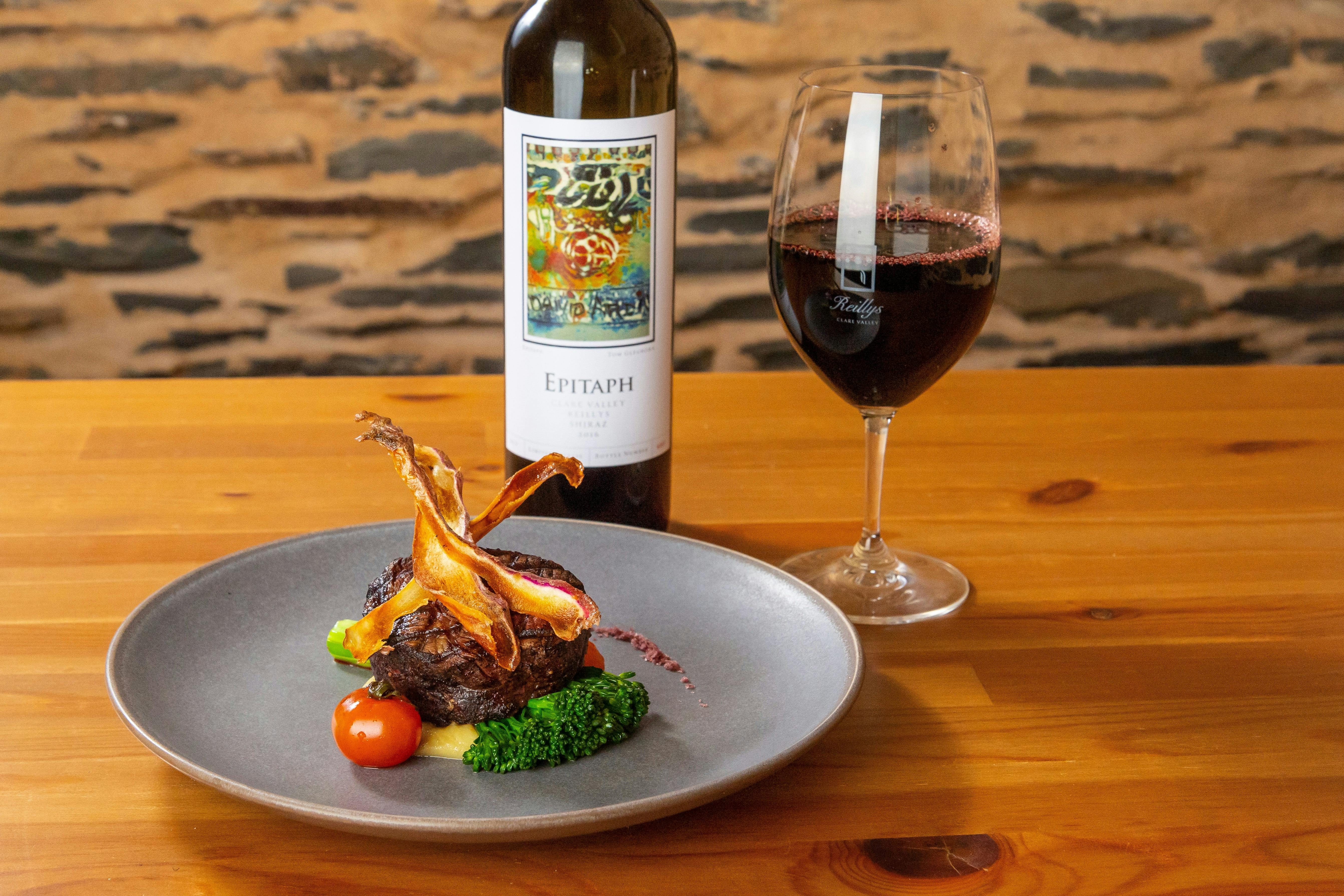 Porterhouse steak garnished won a grey plate with a bottle and glass of red wine behind on the table