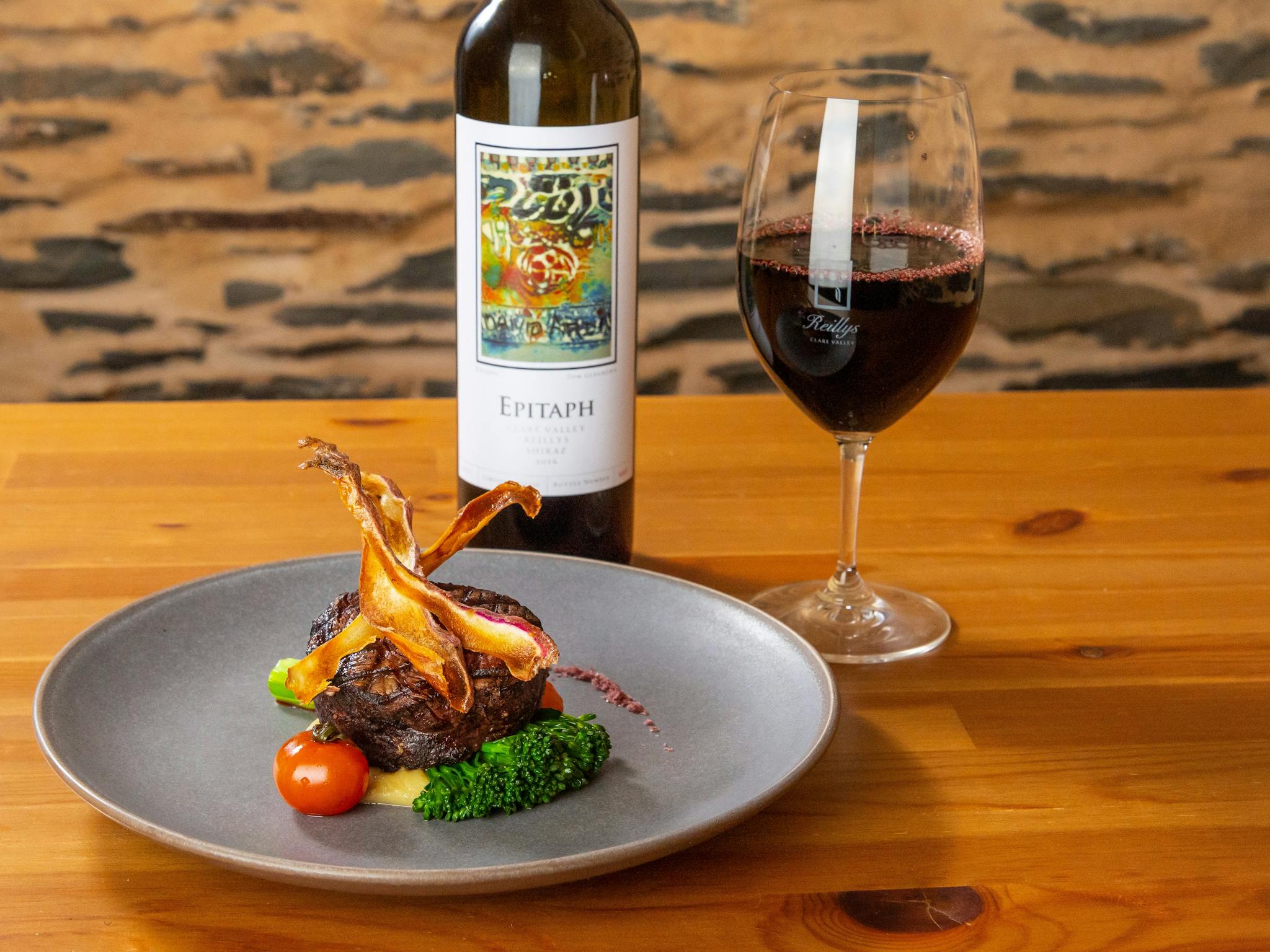 Porterhouse steak garnished won a grey plate with a bottle and glass of red wine behind on the table