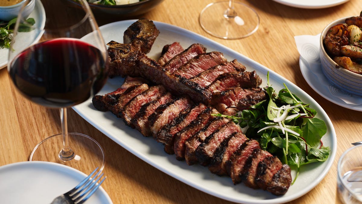 Juicy premium T-Bone steak on white plate with salad and glass of red wine at Hurricane's Grill.