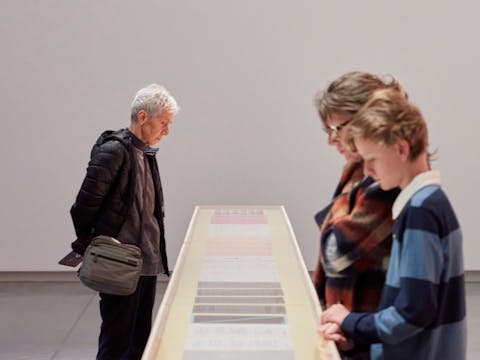 Three visitors in Bundanon's Art Museum looking at a table display of contemporary art