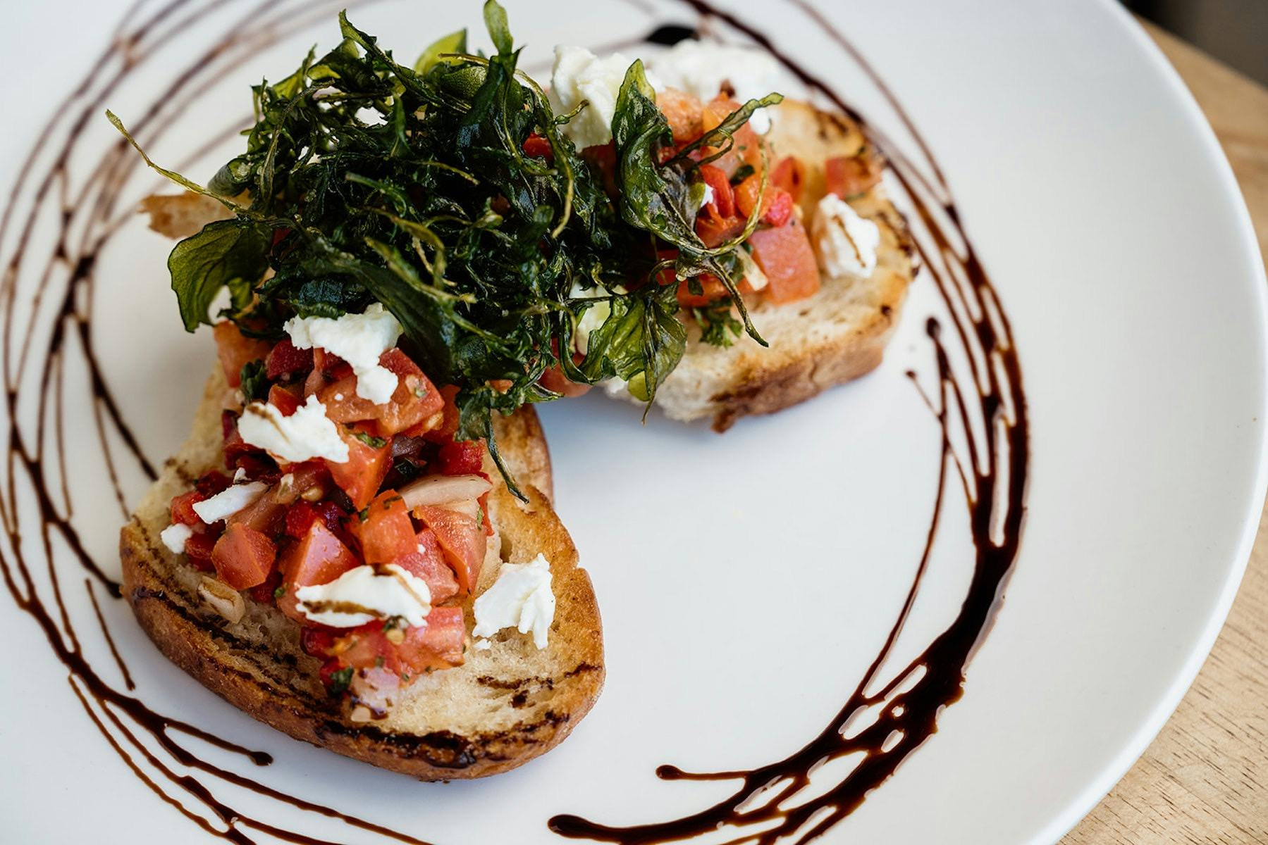 Two slices of Bruschetta, served on a plate with a swirl of Balsamic Glaze.