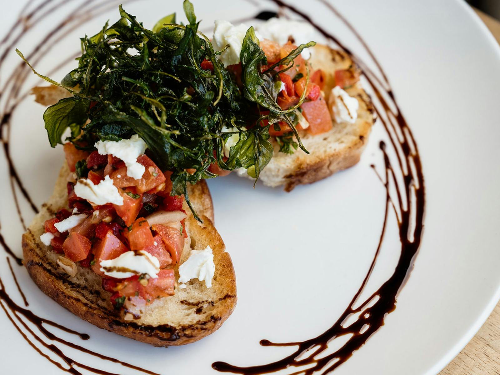 Two slices of Bruschetta, served on a plate with a swirl of Balsamic Glaze.