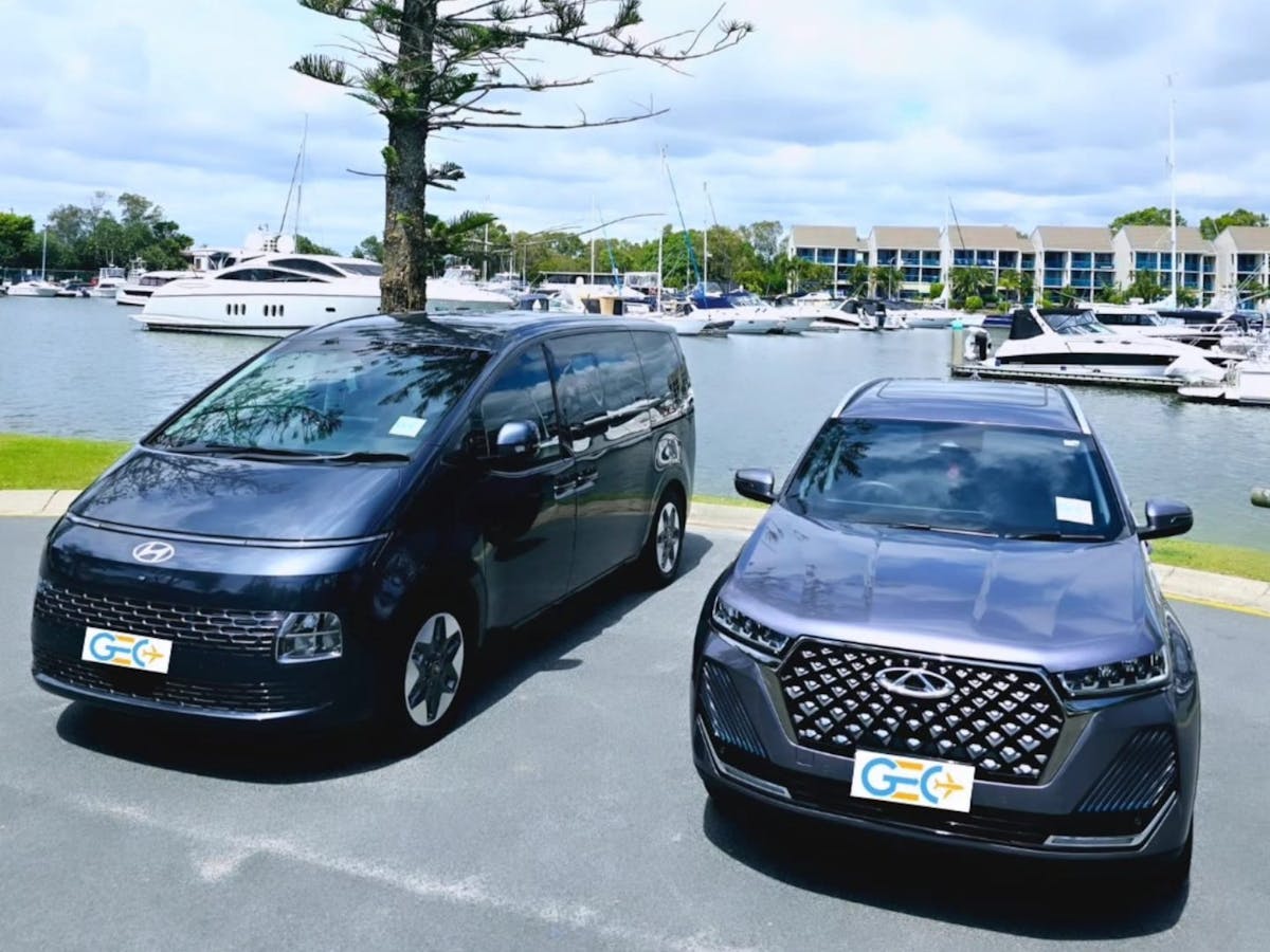 Hyundai van and Chery SUV from GEC Transfers parked near a marina with yachts and waterfront