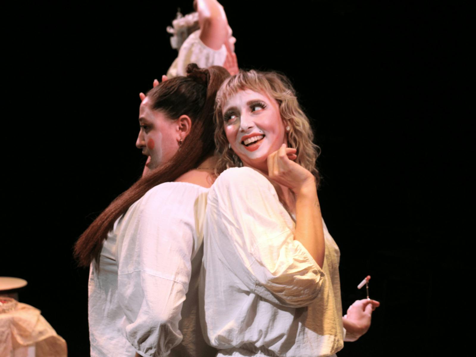 Two women with painted white faces and white blouses pose back-to-back smiling.