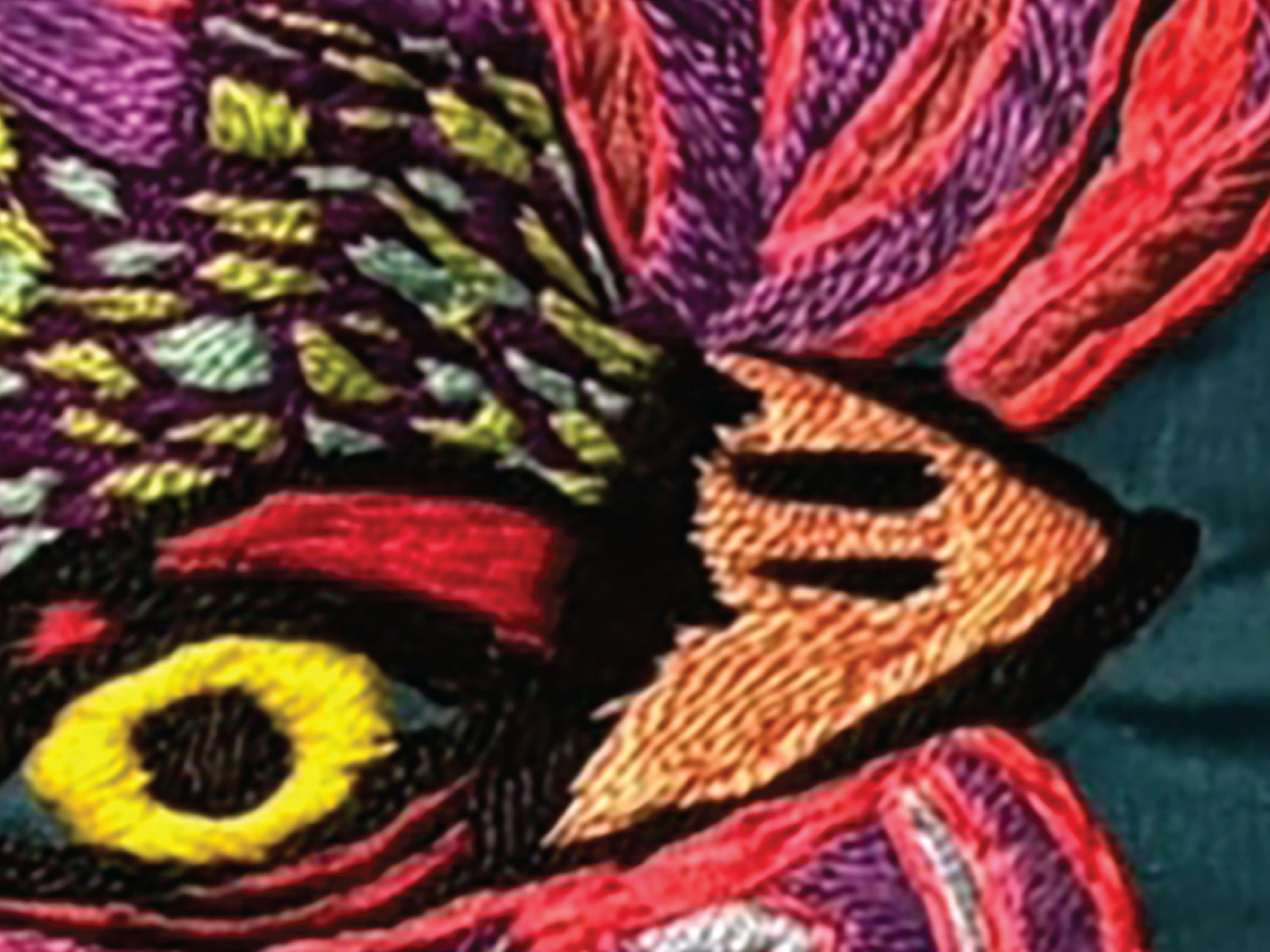 A brightly coloured bird in red, purple, and green with a yellow eye. Embroidery on fabric