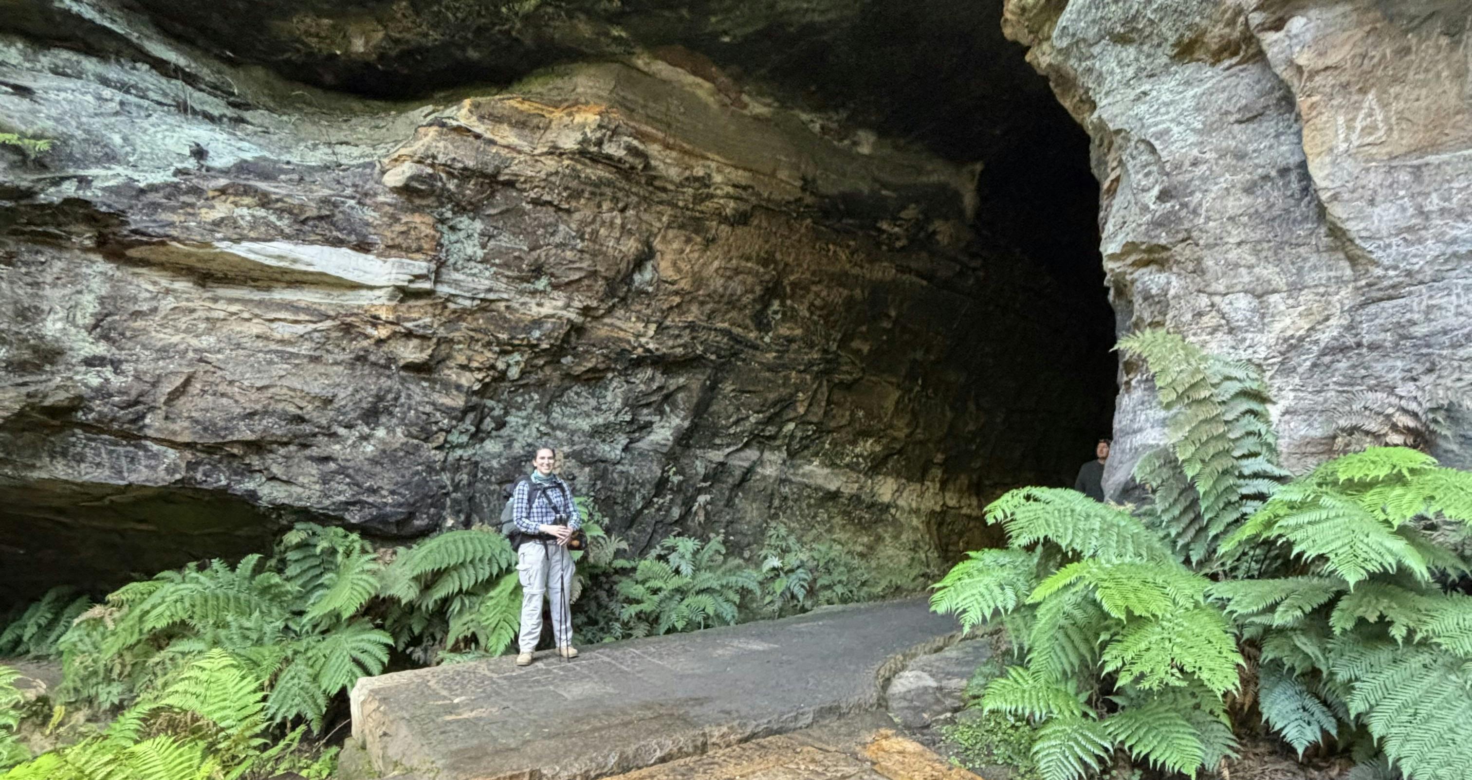 Woman wearing grey pants and checkered shirt standing next to an old, disused railway tunnel.