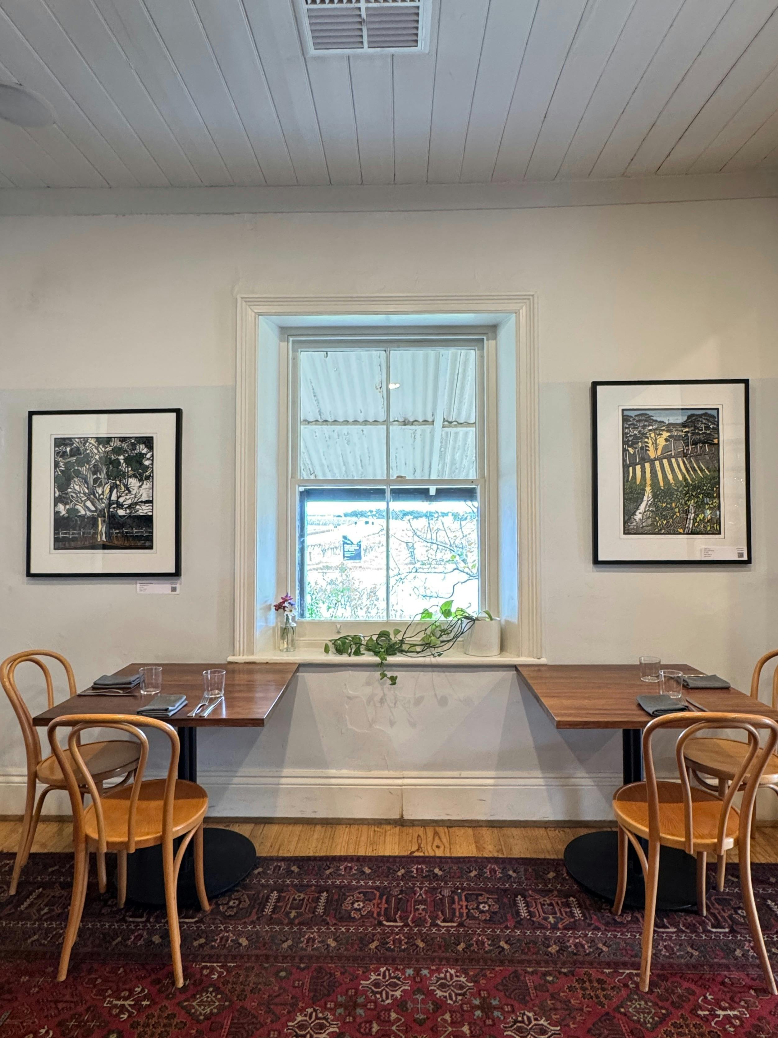 @ framed pictures on either side of a window with tables and chairs