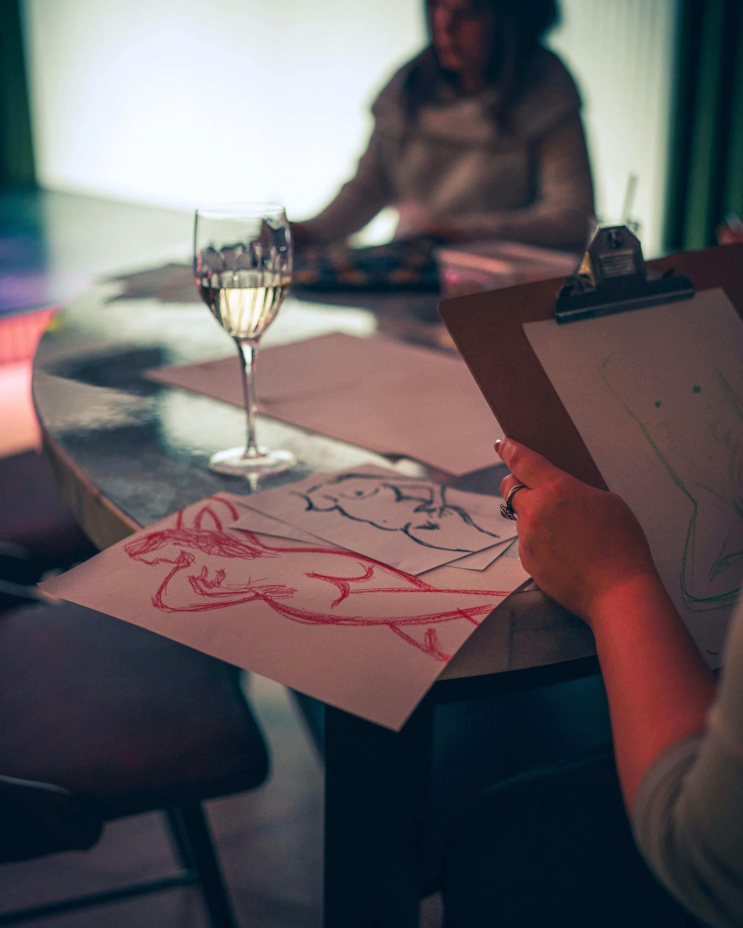 Drawing of naked humans next to a glass of wine