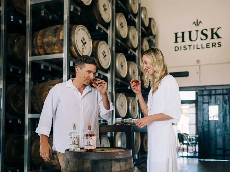 A man and a woman wine tasting gin and rum on a barrel at Husk Farm Distillery.