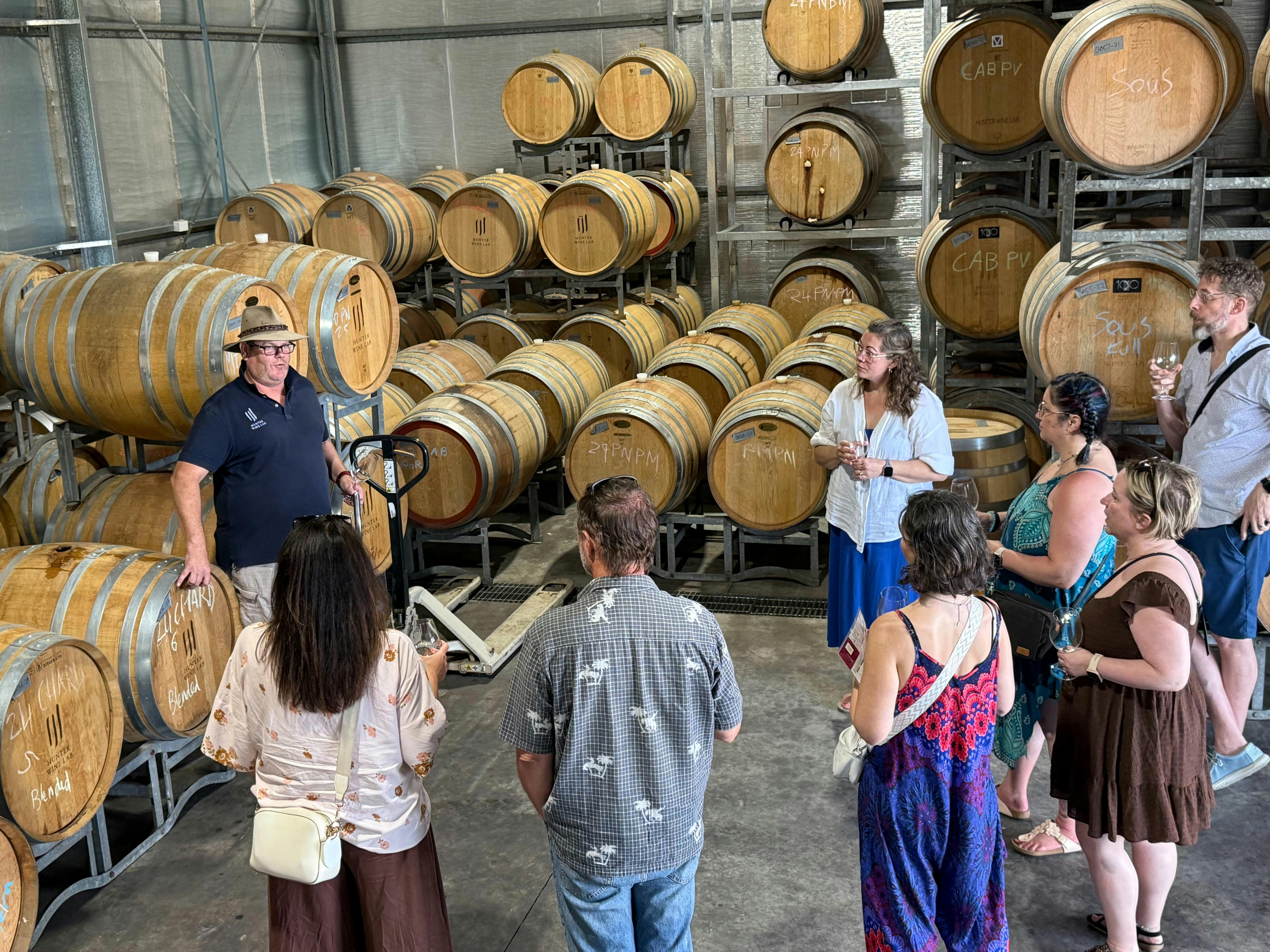 Guests standing in front of wine barrels during a winery tour at Hunter Wine Lab.