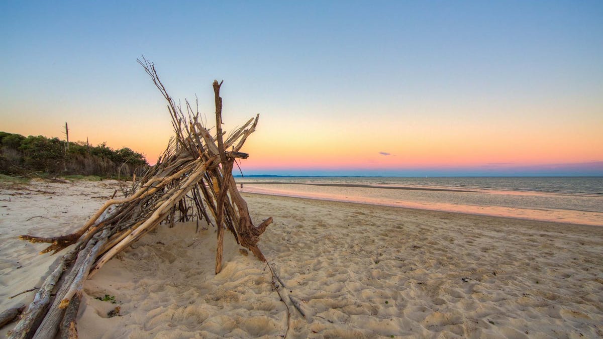 Large triangular tent made out of sticks and branches on the beach at sunset
