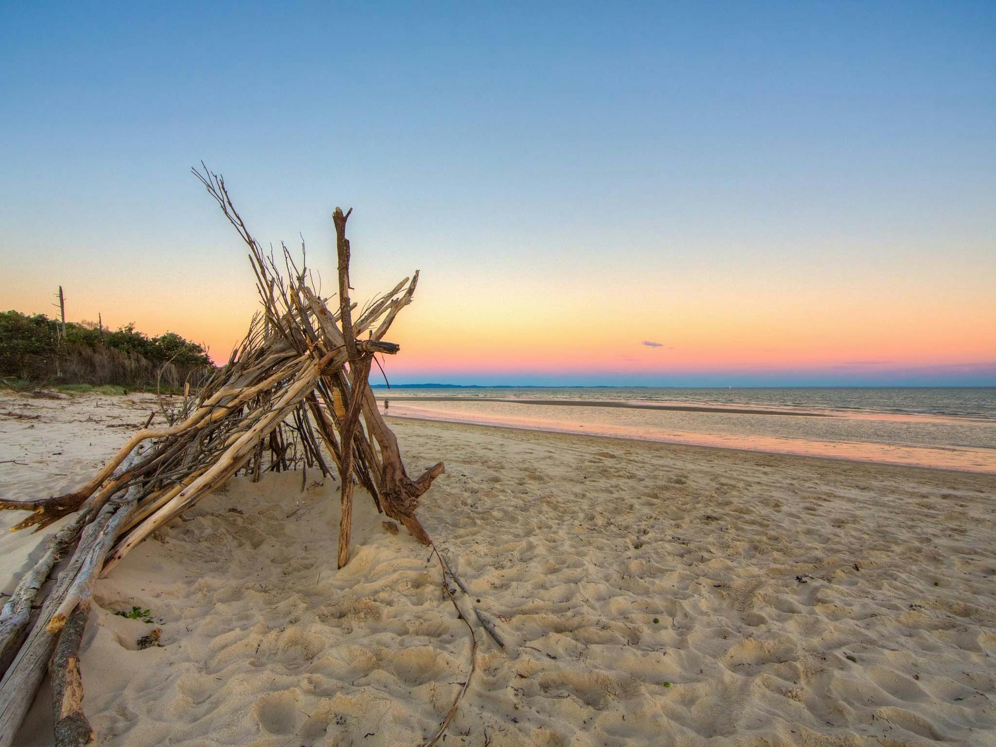 Large triangular tent made out of sticks and branches on the beach at sunset Large triangular tent made out of sticks and branches on the beach at sunset
