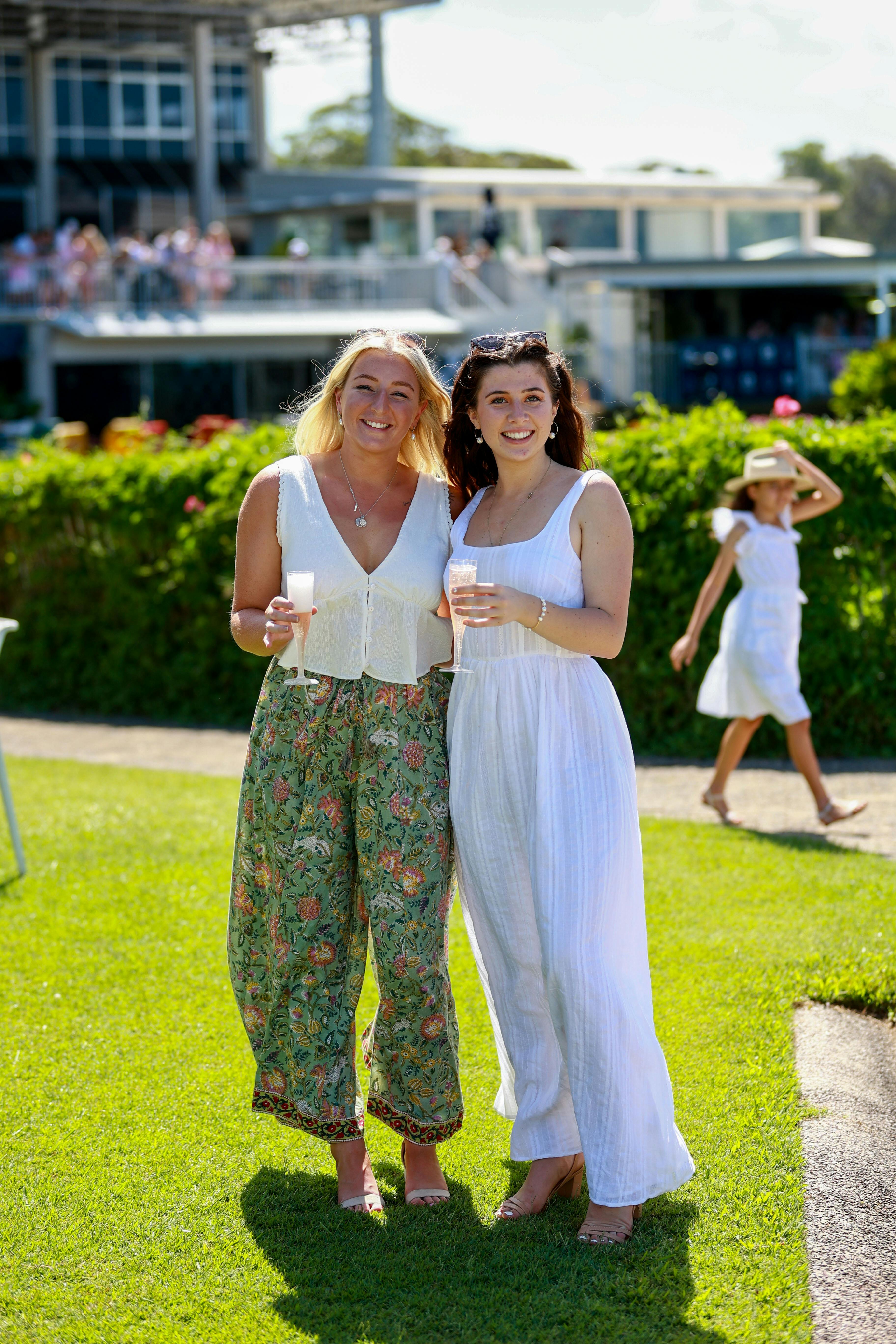 Two girl friends holding champagne on the front lawn and smiling at the camera