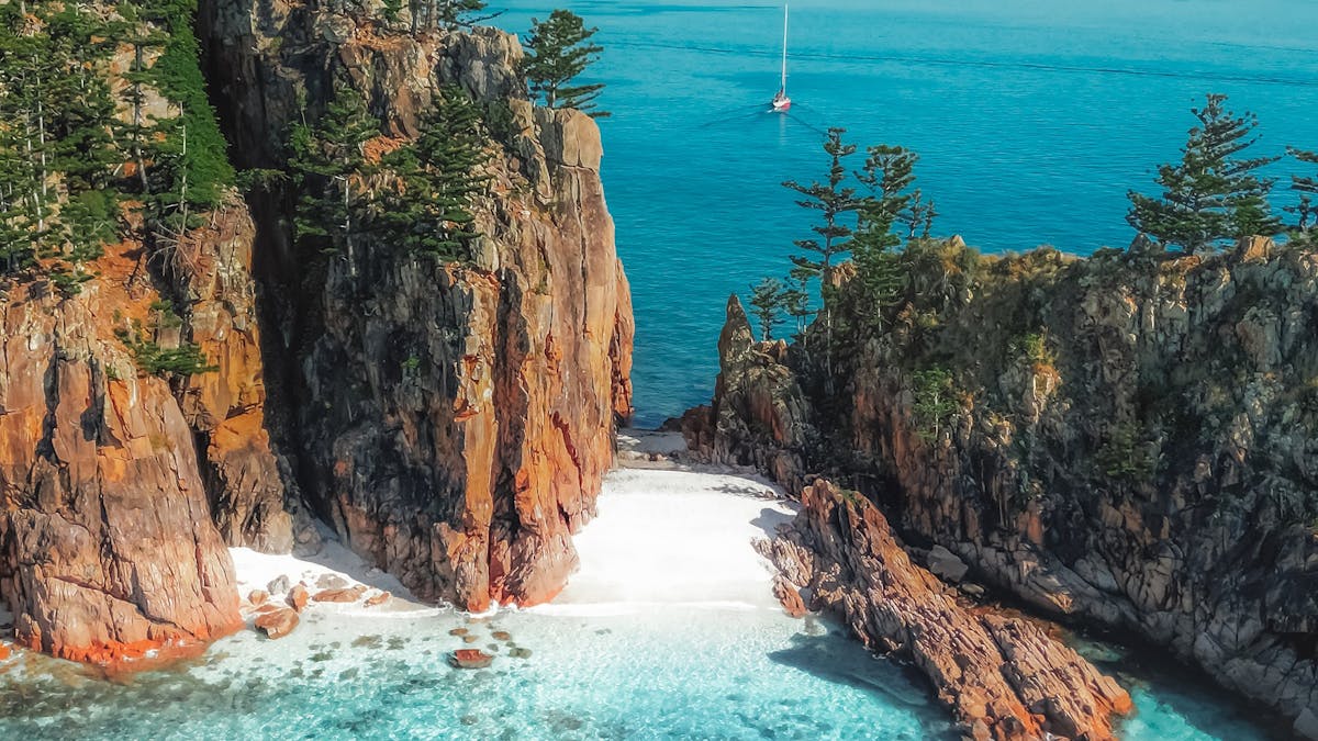 Aerial view of a secluded white-sand beach between rugged cliffs and clear blue ocean
