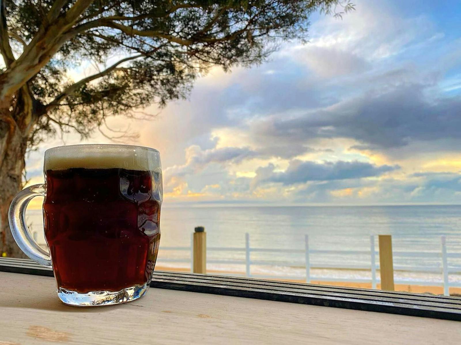 A glass of beer with a beautiful ocean view behind it