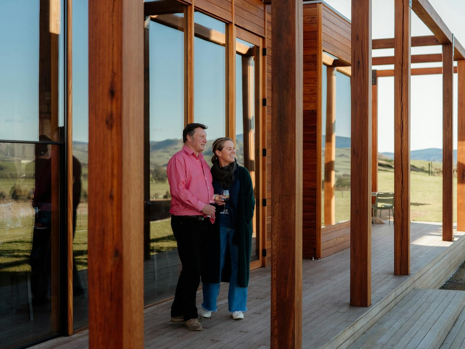 Two people standing on the deck in front of the cellar door holding glasses of wine.
