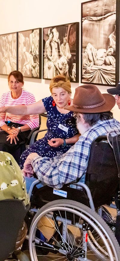 A group of people, some in wheelchairs, sit around a sculpture listening to a guide