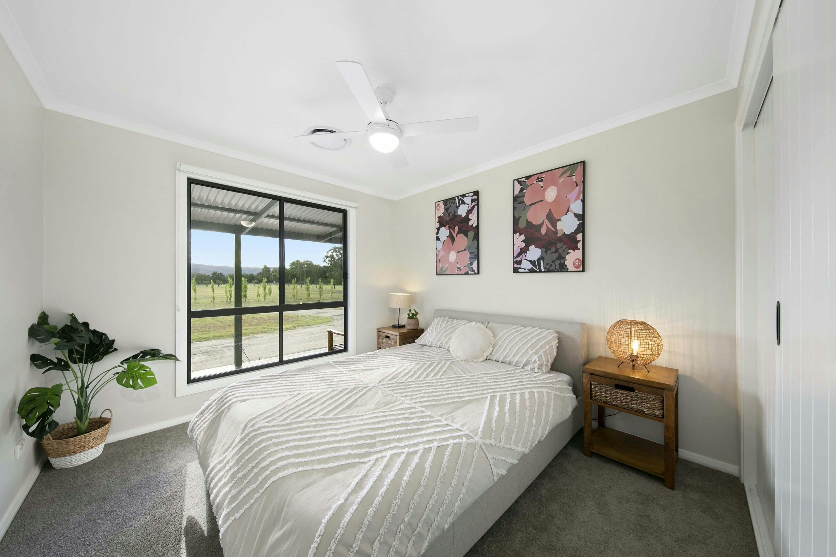 bedroom with a large window, double bed with patterned white bedding, two framed floral artworks